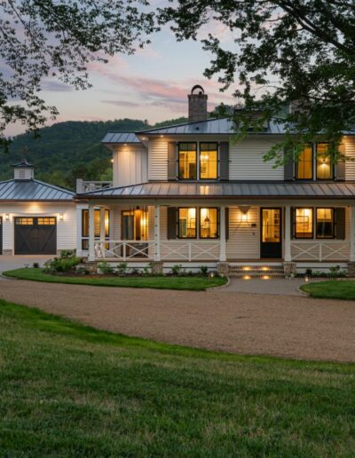 Elegant farmhouse entrance boasting columns, a rustic wood door, and scenic farmland in the backdrop.