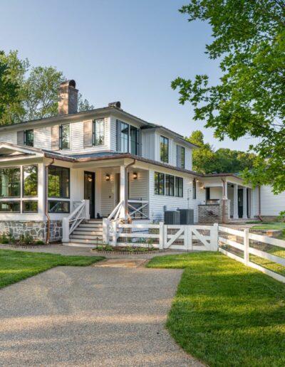 Idyllic farmhouse retreat showcasing a wrap-around porch, flowerbeds, and serene natural surroundings.